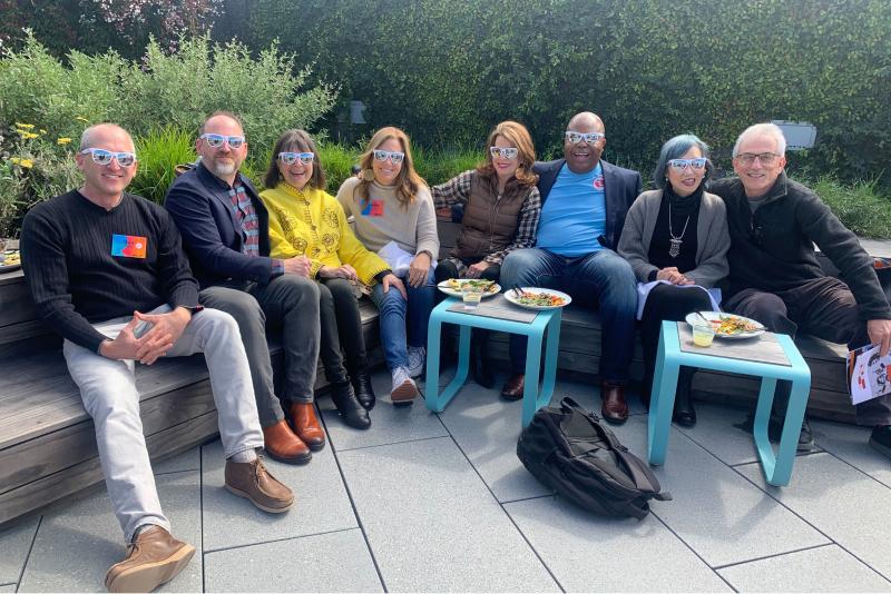 A group of adults wearing sunglasses sit outdoors